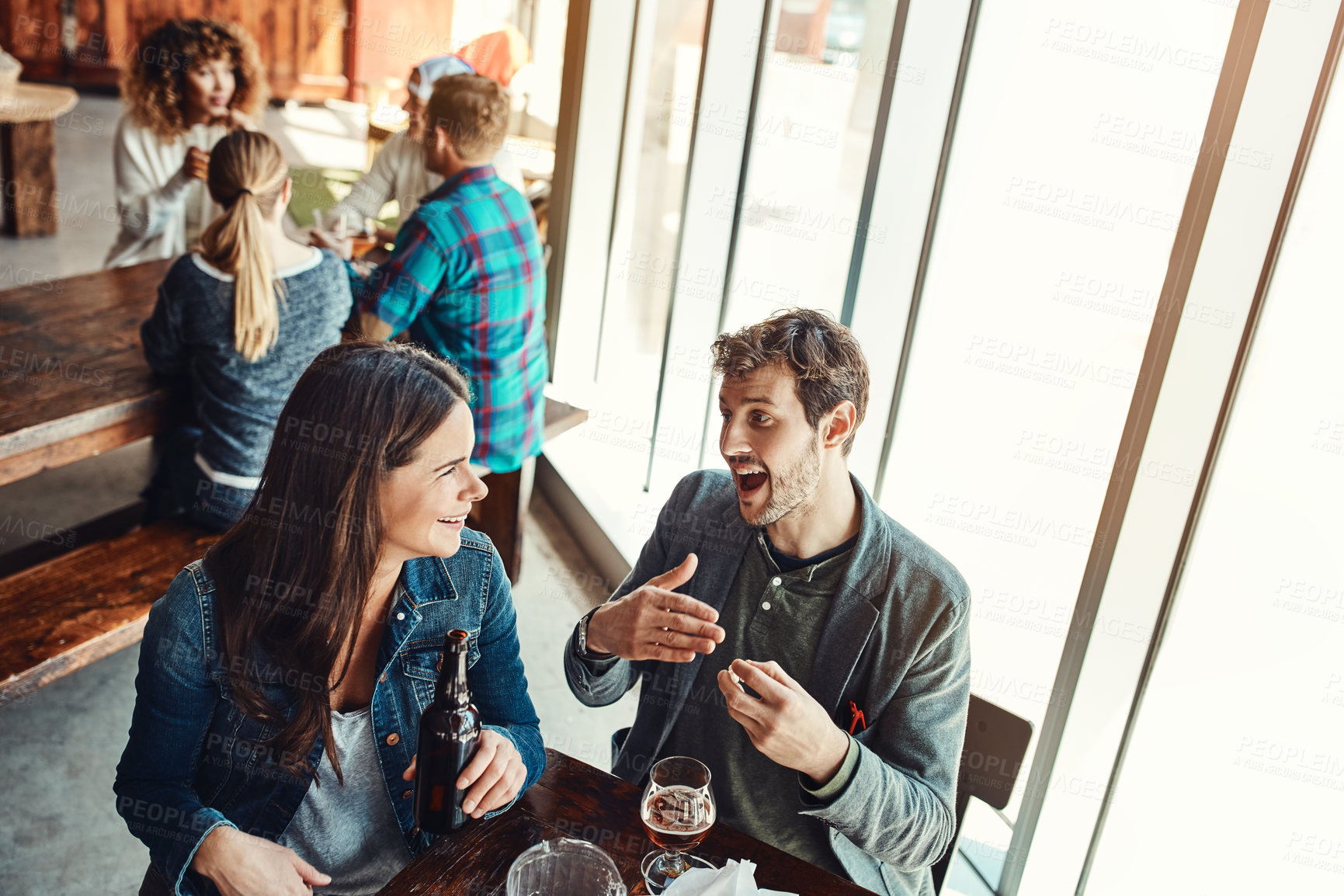 Buy stock photo Cropped shot of a young couple having drinks in a bar with people blurred in the background