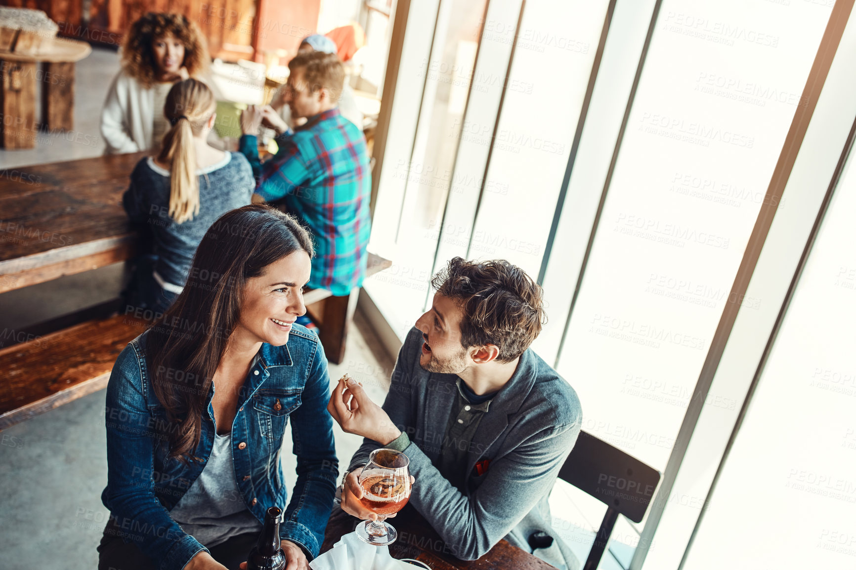 Buy stock photo Cropped shot of a young couple having drinks in a bar with people blurred in the background