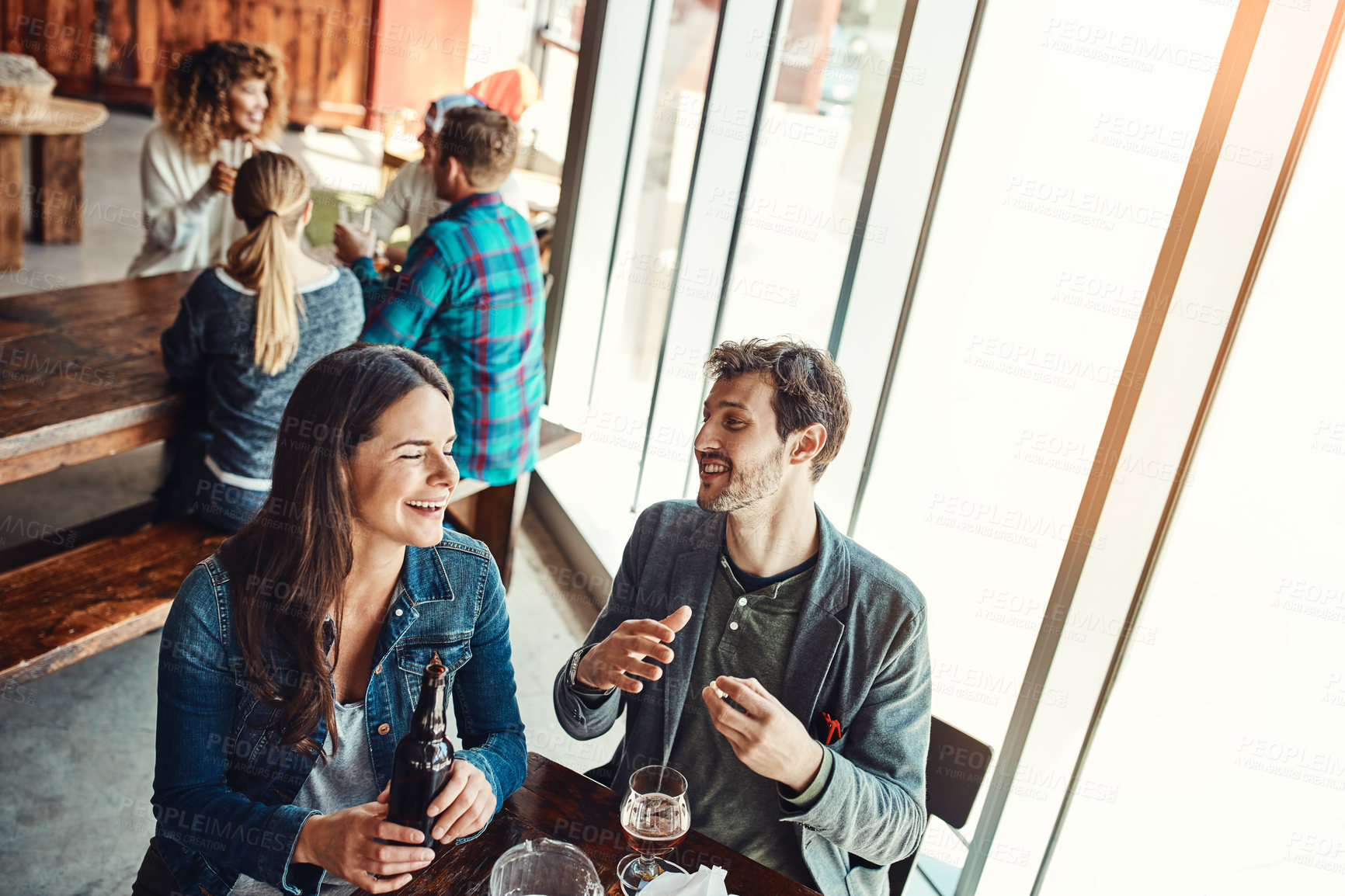 Buy stock photo Cropped shot of a young couple having drinks in a bar with people blurred in the background