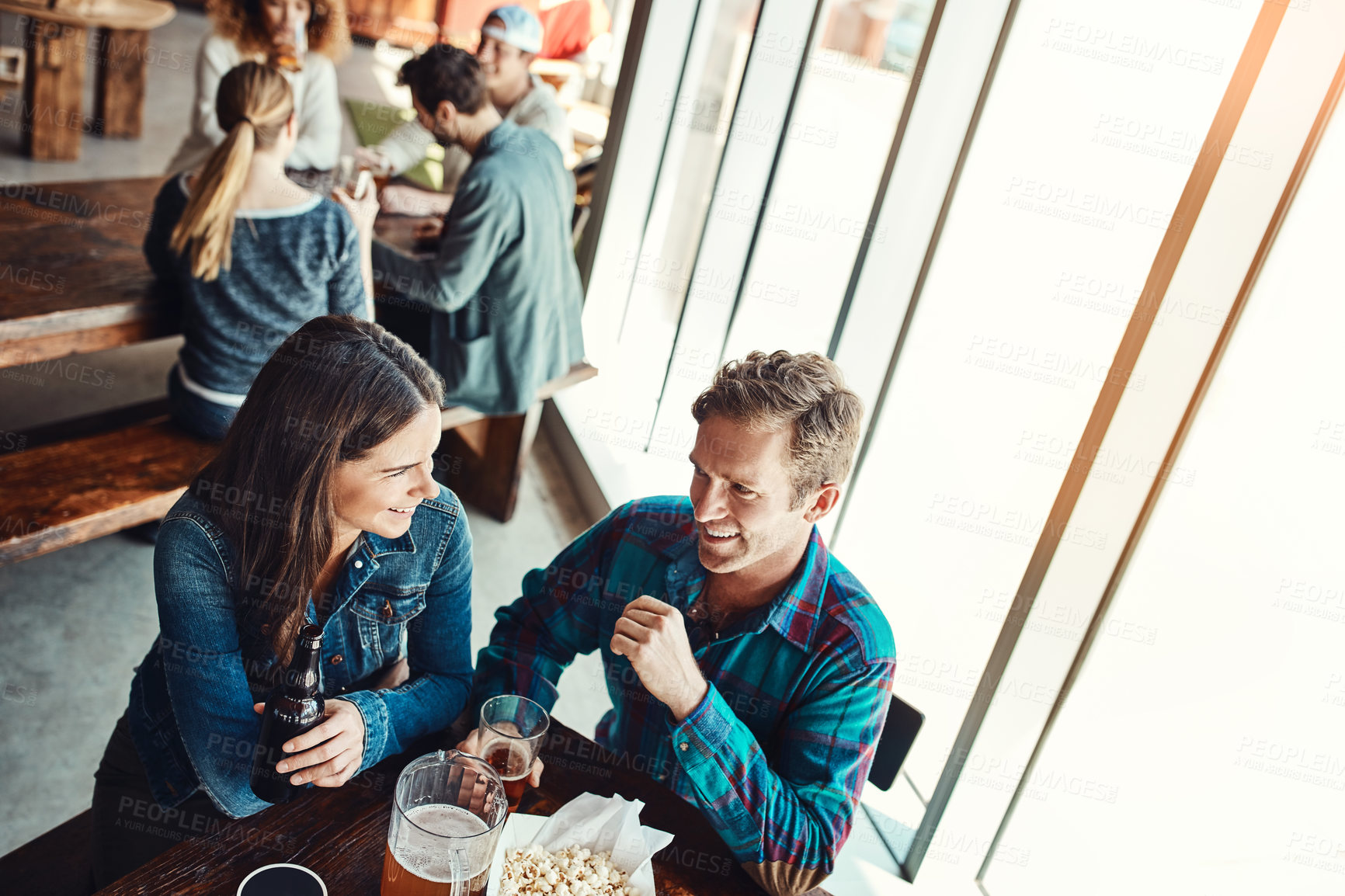 Buy stock photo Cropped shot of a young couple having drinks in a bar with people blurred in the background