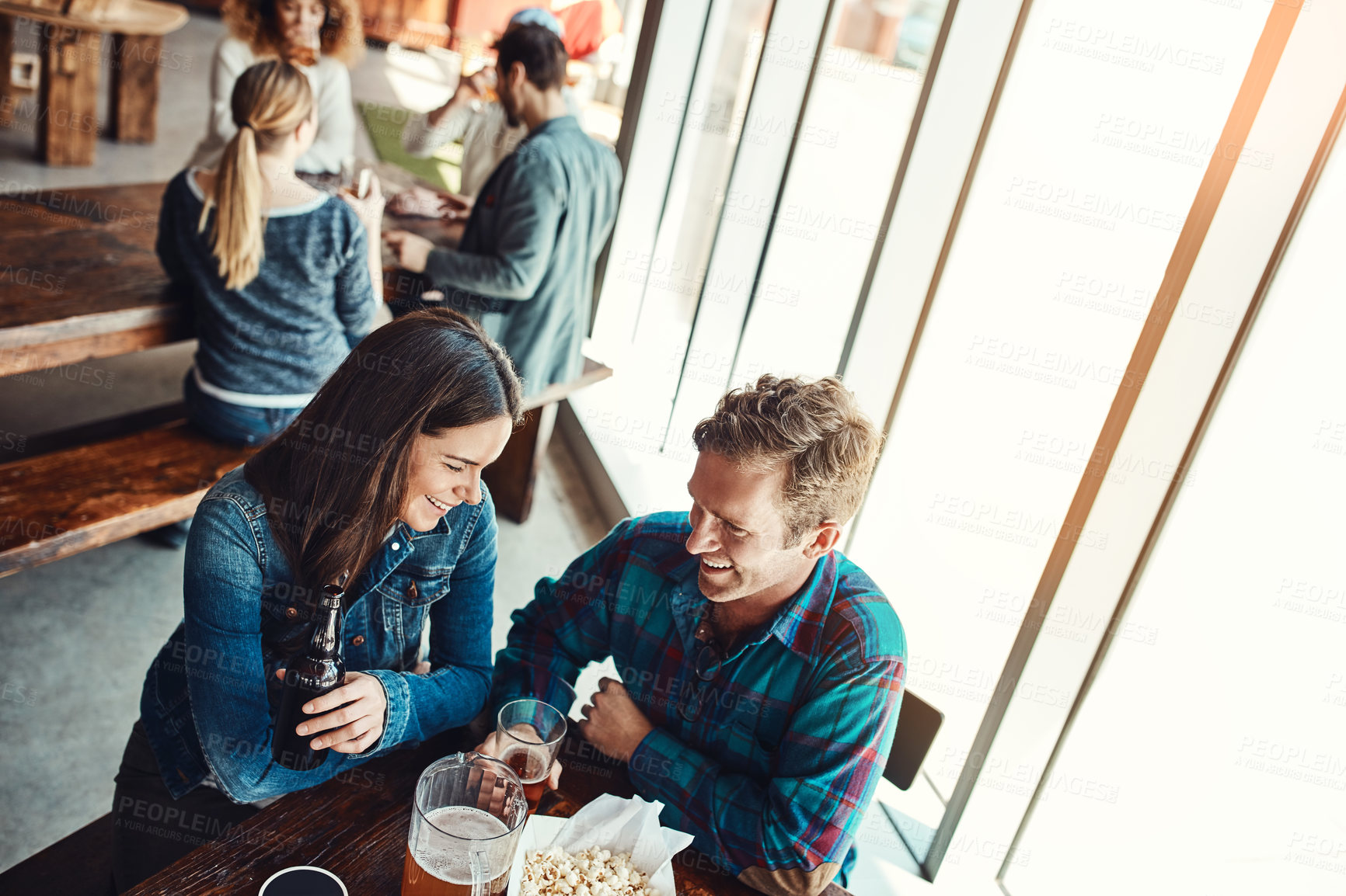 Buy stock photo Cropped shot of a young couple having drinks in a bar with people blurred in the background