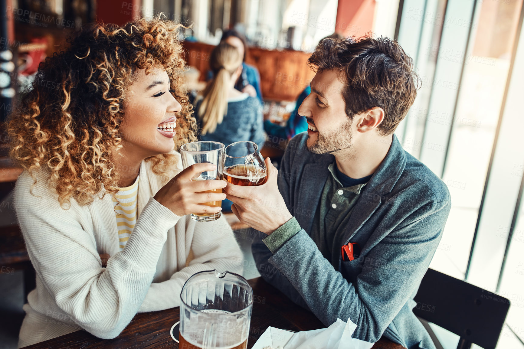 Buy stock photo Cropped shot of a young couple having drinks in a bar with people blurred in the background