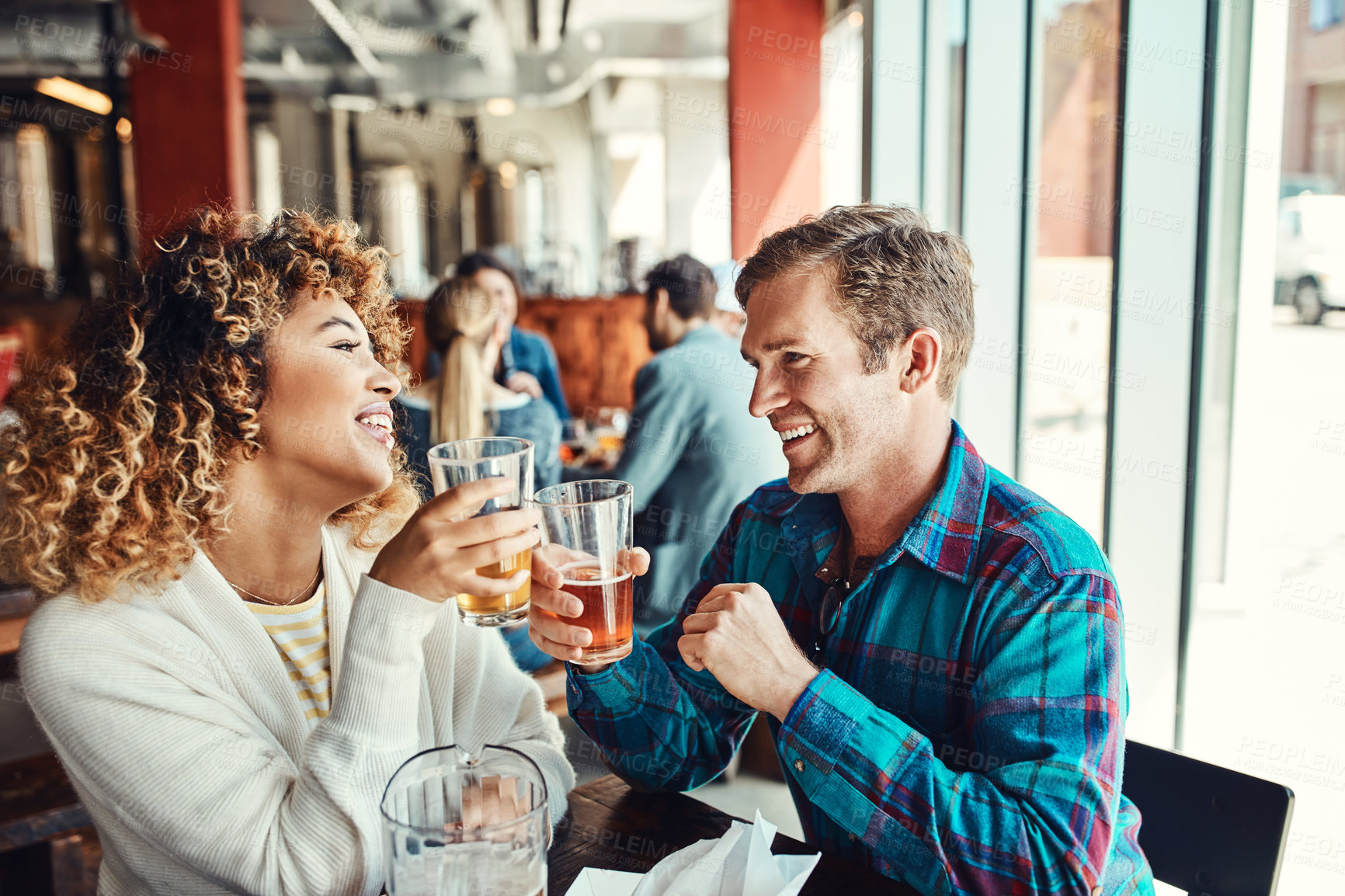 Buy stock photo Cropped shot of a young couple having drinks in a bar with people blurred in the background