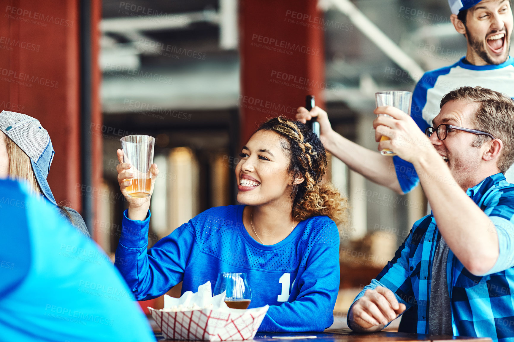 Buy stock photo Shot of a group of friends cheering while watching a sports game at a bar