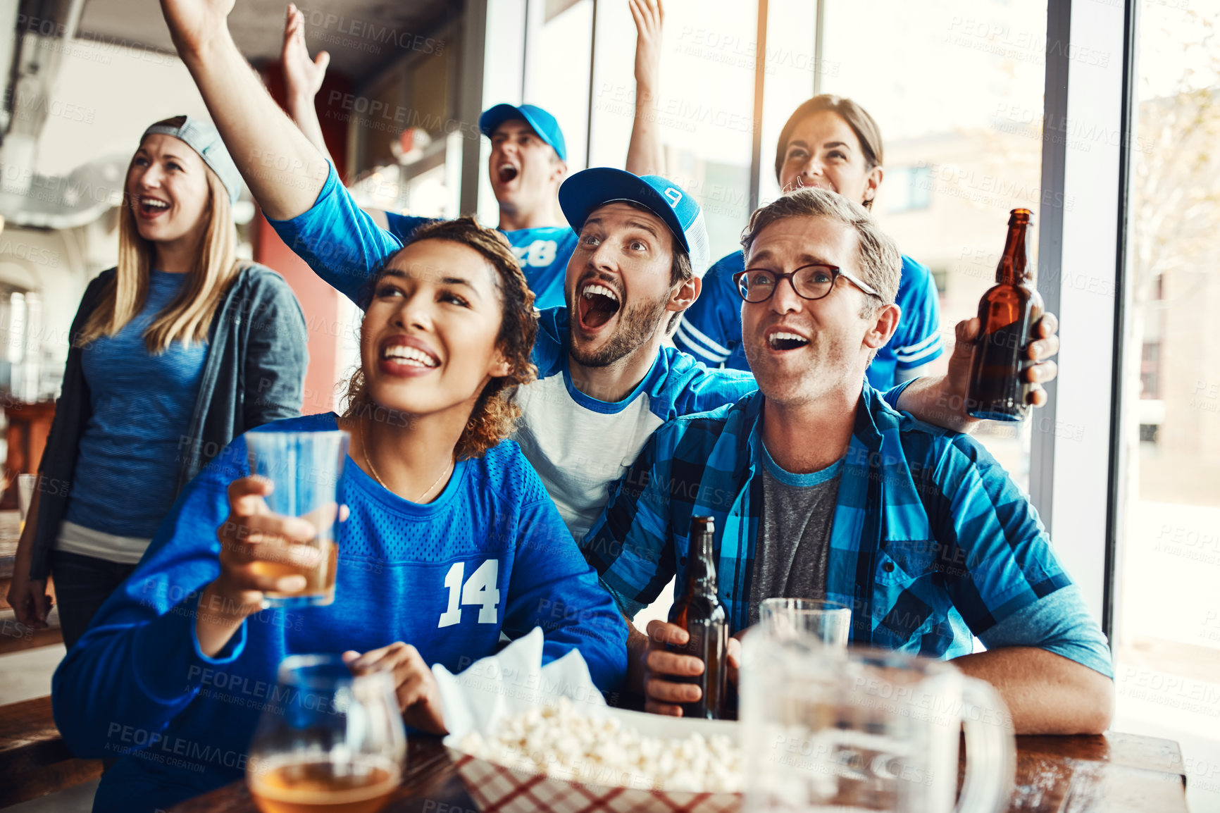 Buy stock photo Shot of a group of friends cheering while watching a sports game at a bar