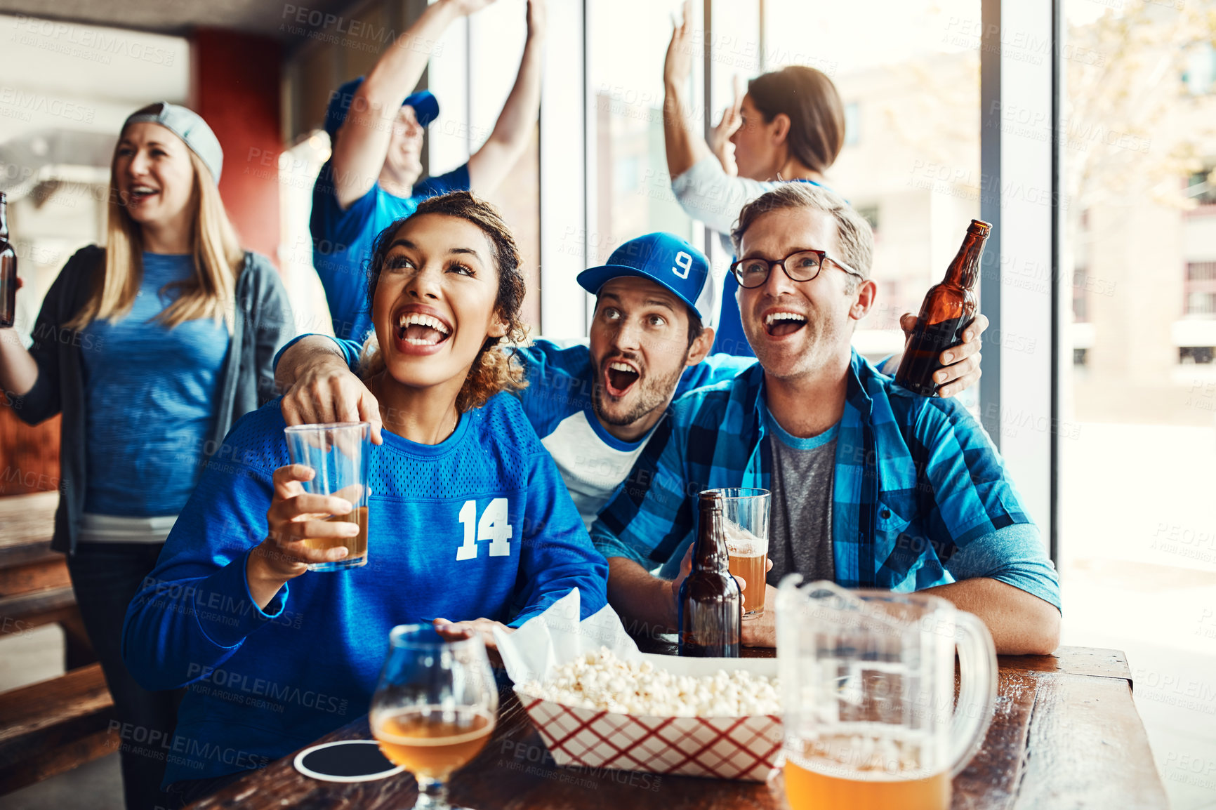 Buy stock photo Shot of a group of friends cheering while watching a sports game at a bar