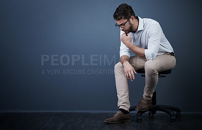 Buy stock photo Studio shot of a handsome young businessman looking thoughtful while sitting on a chair against a dark background