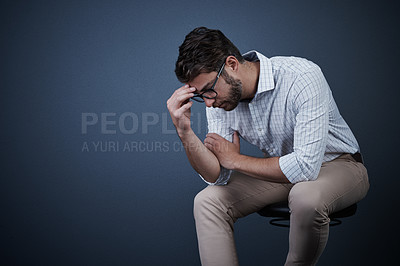 Buy stock photo Studio shot of a handsome young businessman looking stressed while sitting on a chair against a dark background