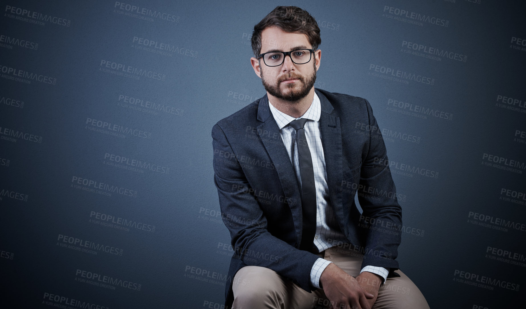 Buy stock photo Studio portrait of a handsome young businessman sitting on a chair against a dark background