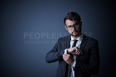 Buy stock photo Studio portrait of a handsome young businessman adjusting his cuffs against a dark background