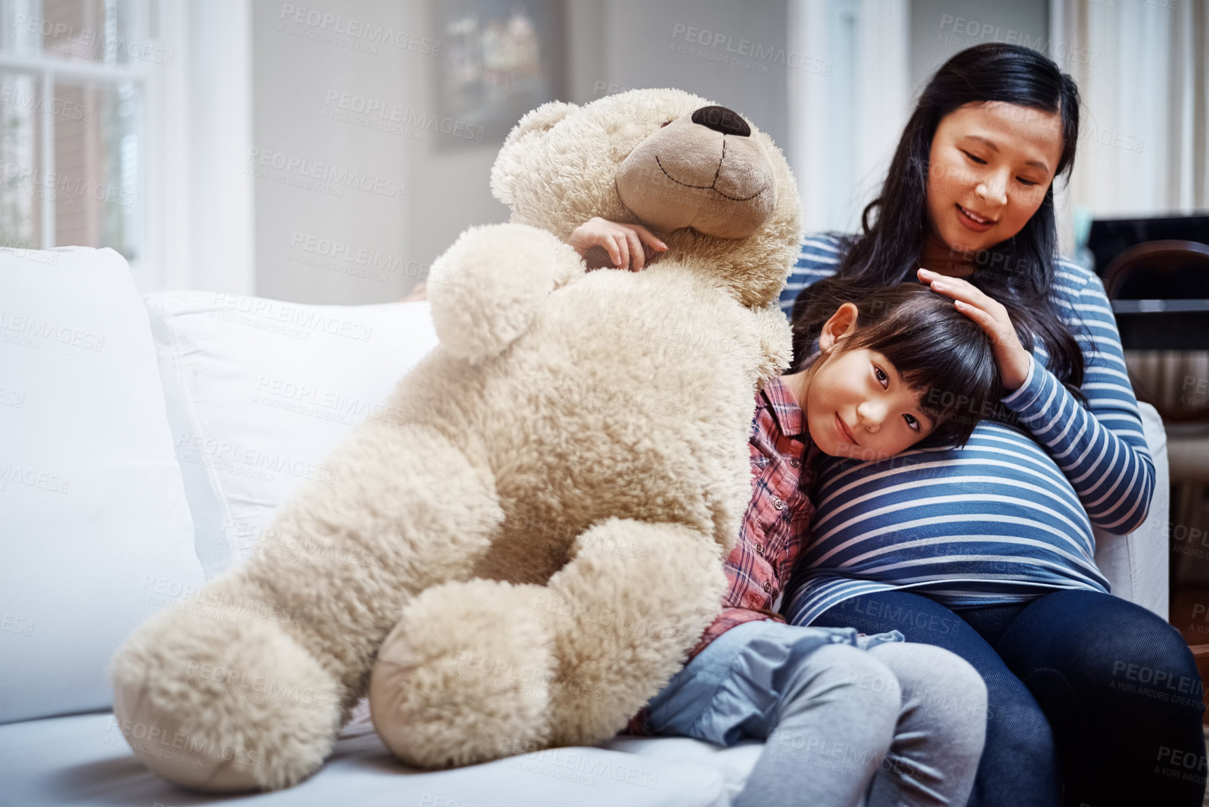 Buy stock photo Cropped portrait of a little girl sitting with her mother and her teddybear on the sofa