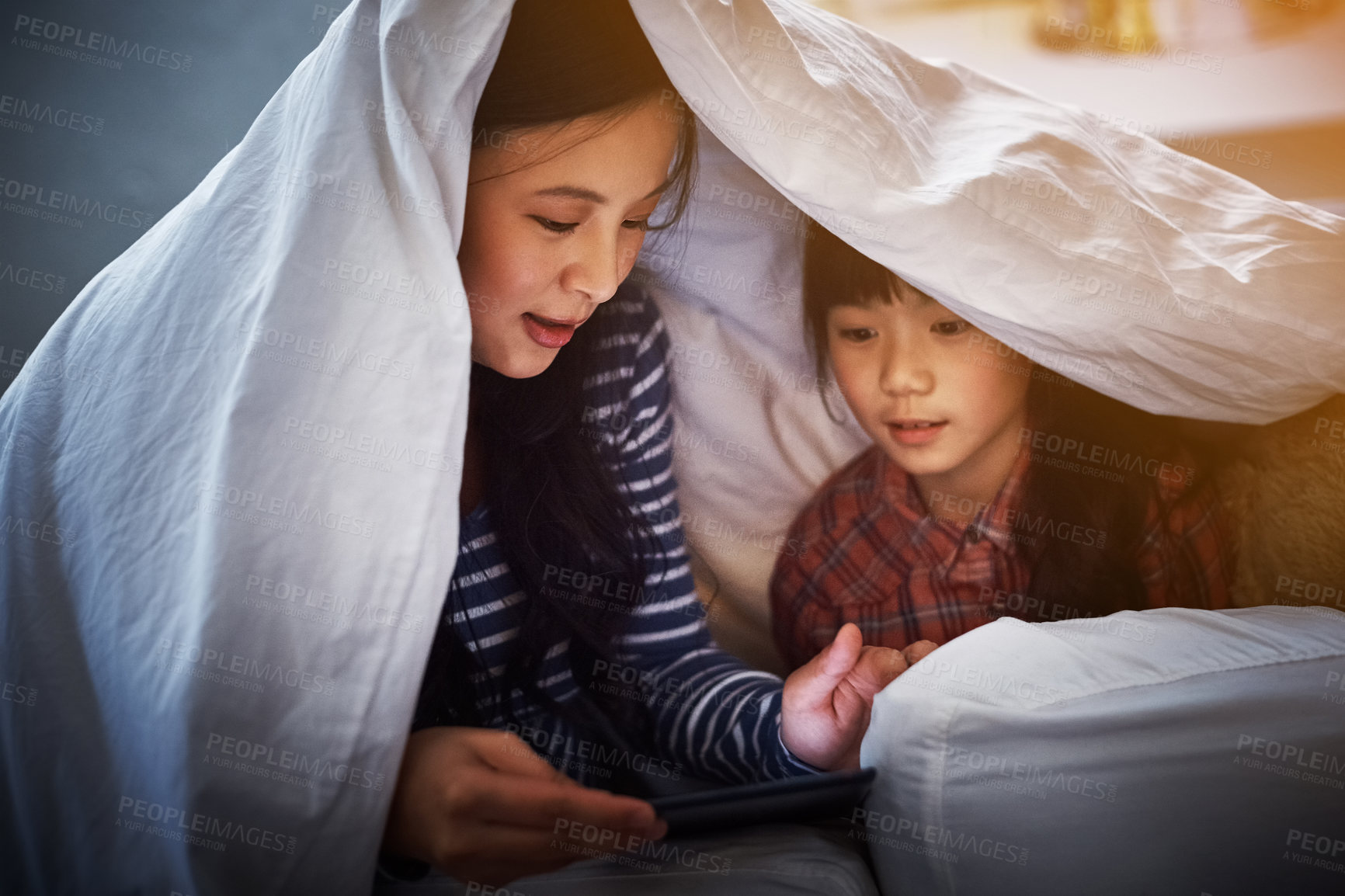 Buy stock photo Cropped shot of an attractive young woman and her daughter using a digital tablet while lying under the covers