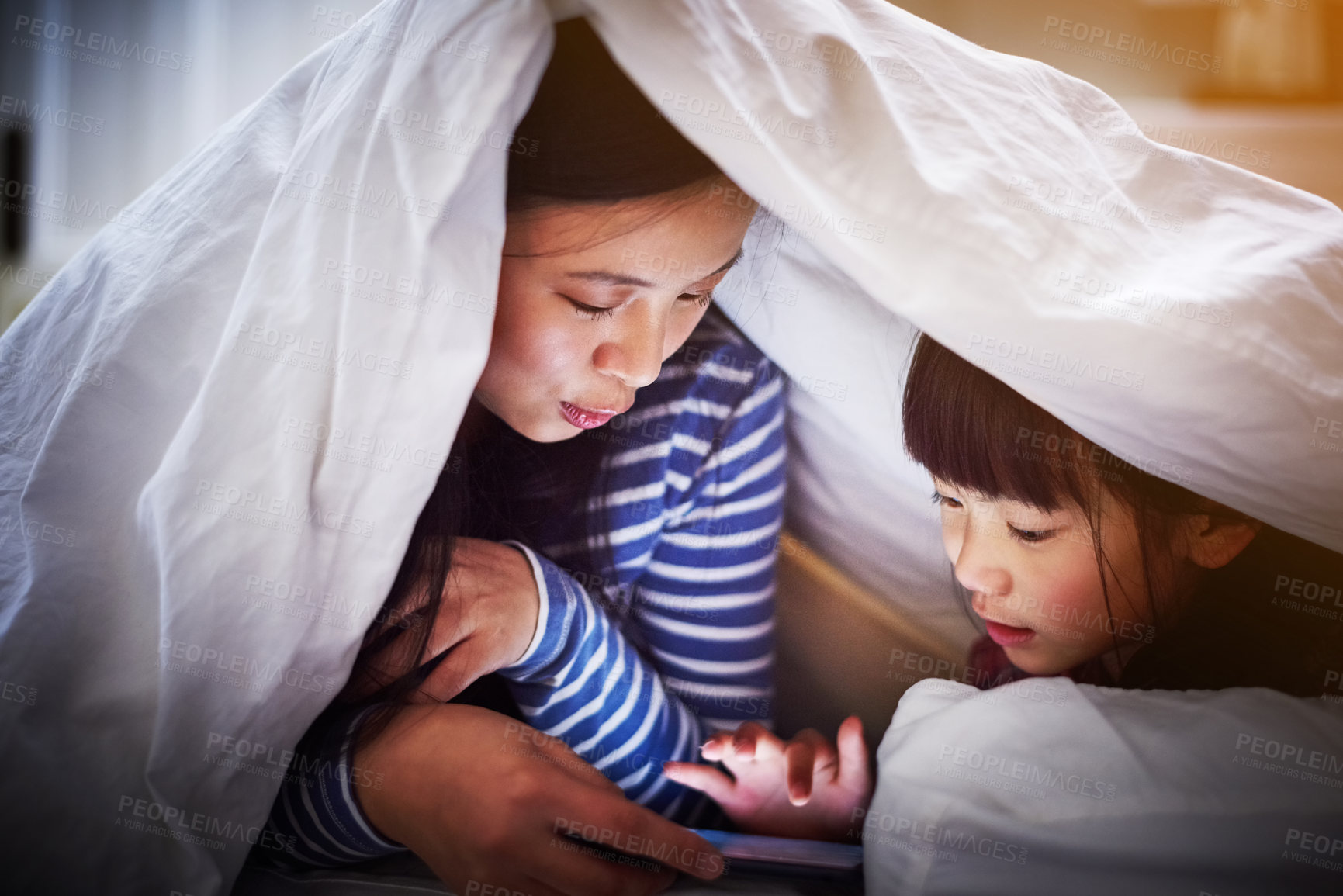 Buy stock photo Cropped shot of an attractive young woman and her daughter using a digital tablet while lying under the covers