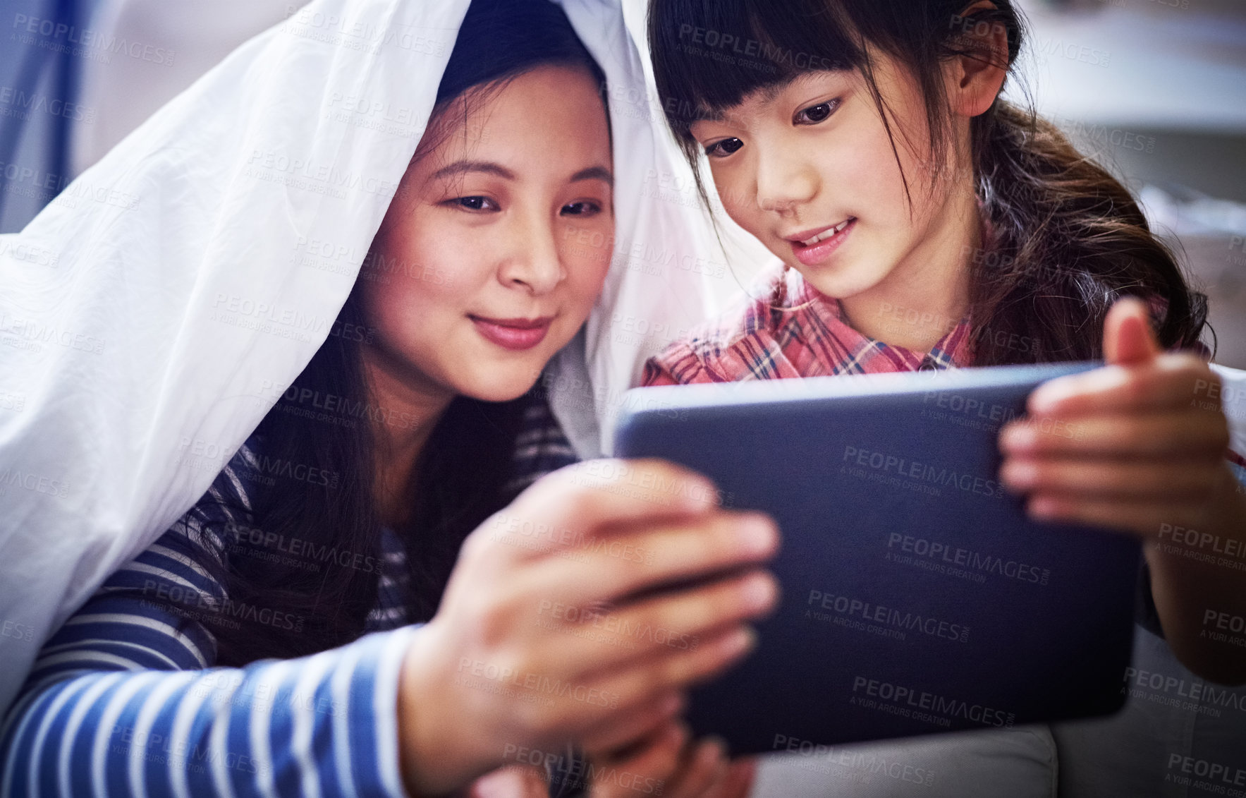 Buy stock photo Cropped shot of an attractive young woman and her daughter using a digital tablet while lying under the covers