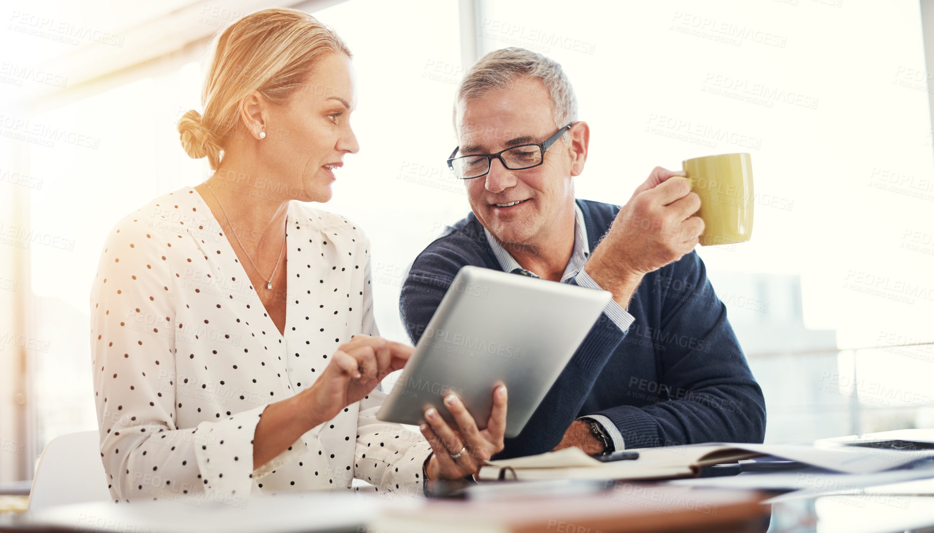 Buy stock photo Shot of a mature couple using a digital tablet while going through paperwork at home