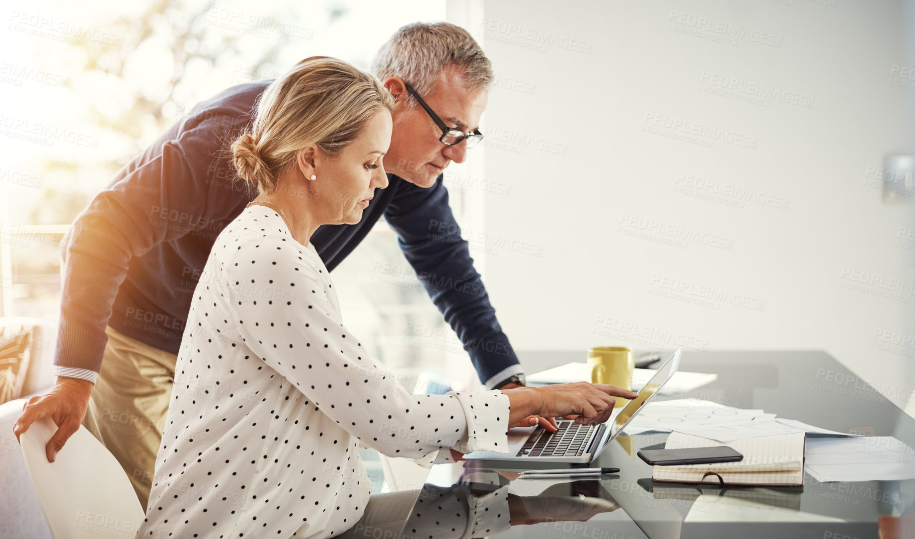 Buy stock photo Shot of a mature couple using a laptop while going through paperwork at home