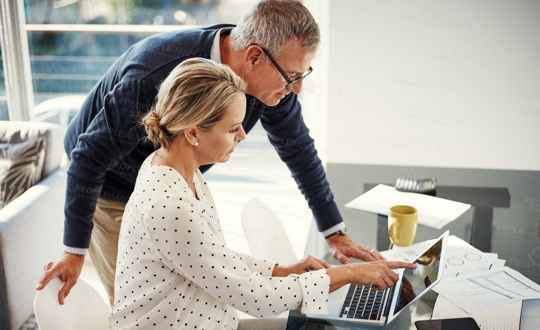 Buy stock photo Shot of a mature couple using a laptop while going through paperwork at home