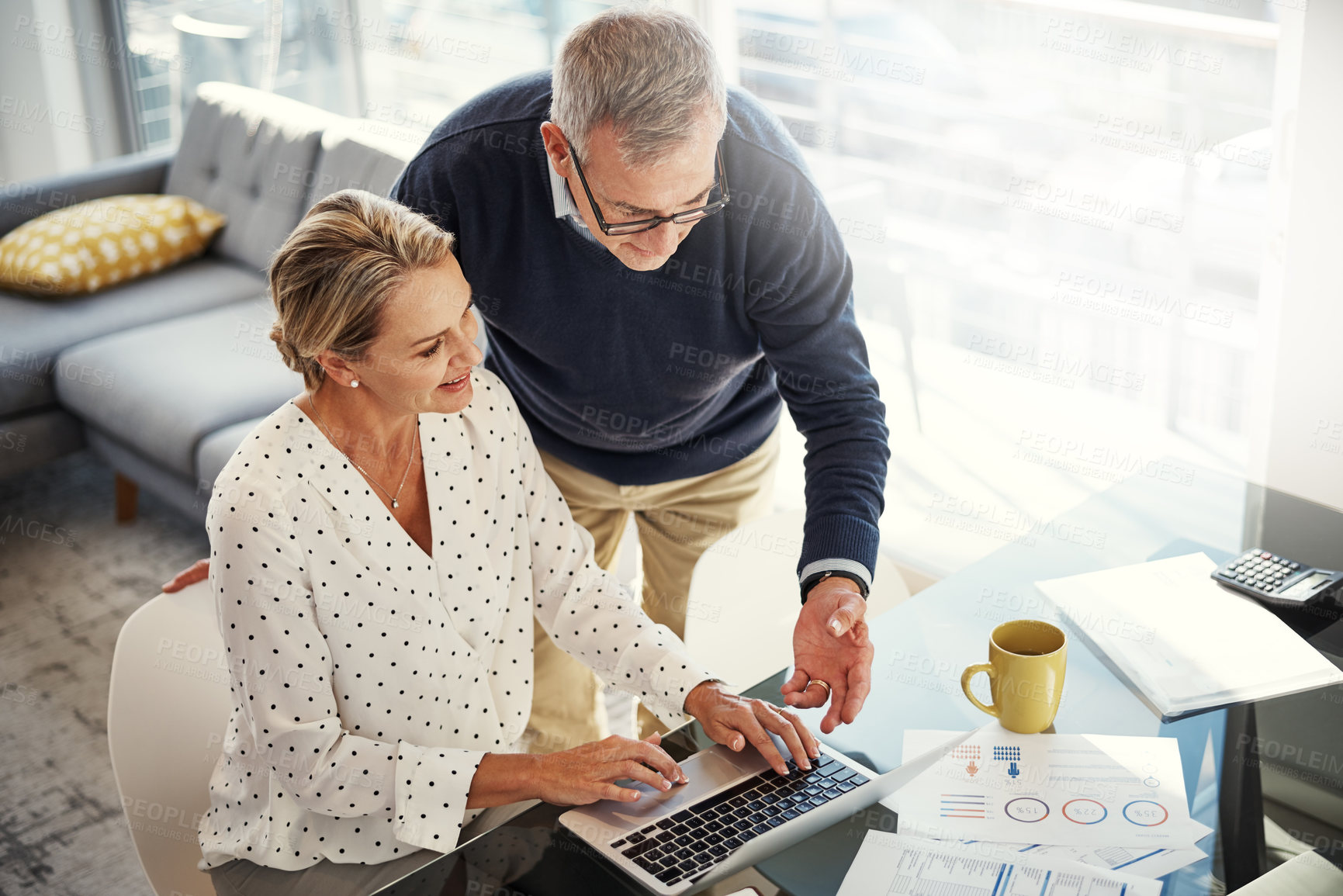 Buy stock photo Shot of a mature couple using a laptop while going through paperwork at home