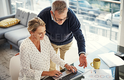 Buy stock photo Shot of a mature couple using a laptop while going through paperwork at home