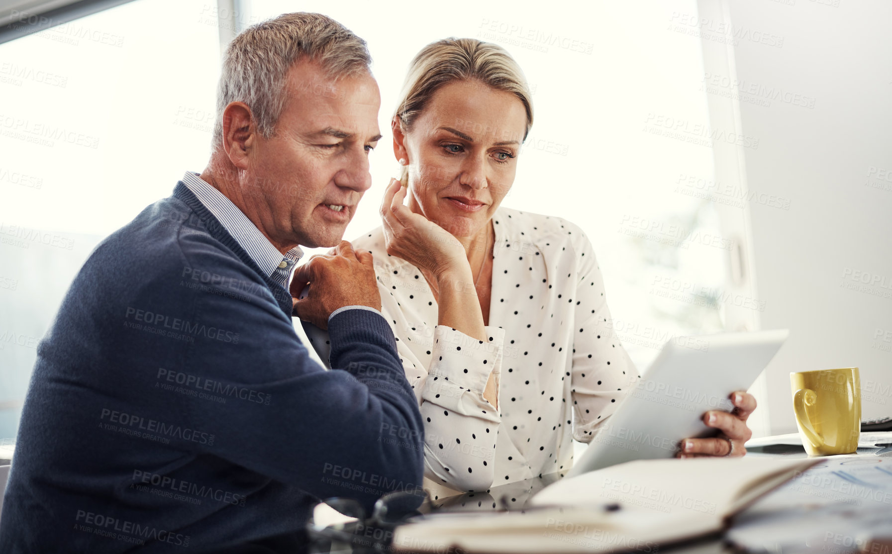 Buy stock photo Shot of a mature couple using a digital tablet while going through paperwork at home