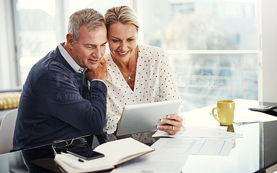 Buy stock photo Shot of a mature couple using a digital tablet while going through paperwork at home