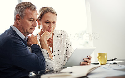 Buy stock photo Shot of a mature couple using a digital tablet while going through paperwork at home