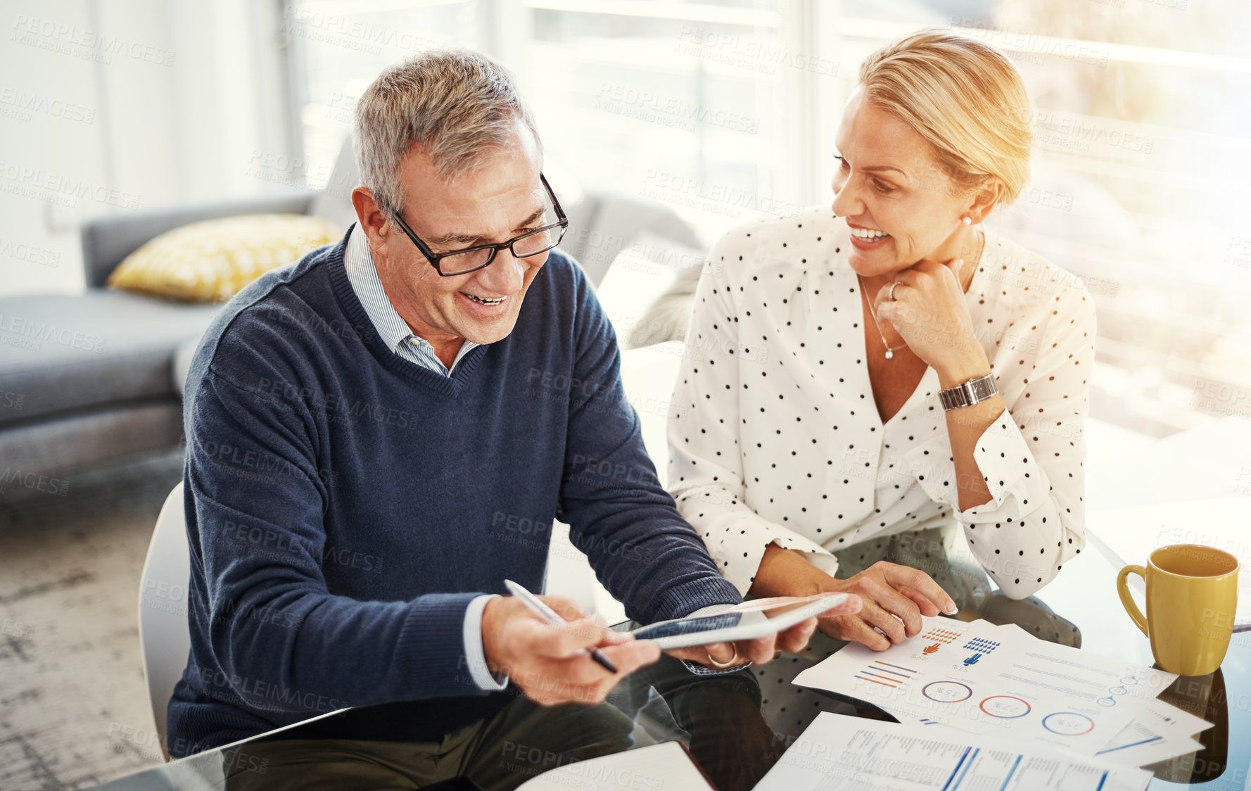 Buy stock photo Shot of a mature couple using a digital tablet while going through paperwork at home