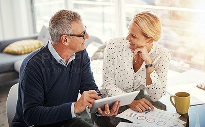 Buy stock photo Shot of a mature couple using a digital tablet while going through paperwork at home