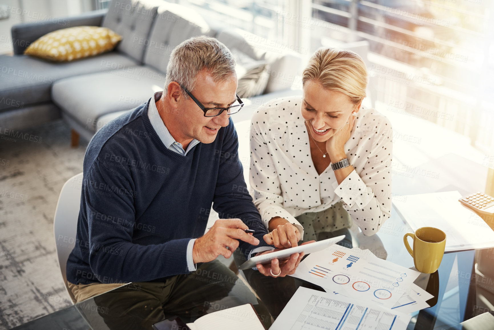 Buy stock photo Shot of a mature couple using a digital tablet while going through paperwork at home