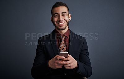 Buy stock photo Studio portrait of a stylish young businessman sending a text message while standing against a gray background