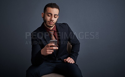 Buy stock photo Studio shot of a stylish young businessman sending a text message while sitting against a gray background