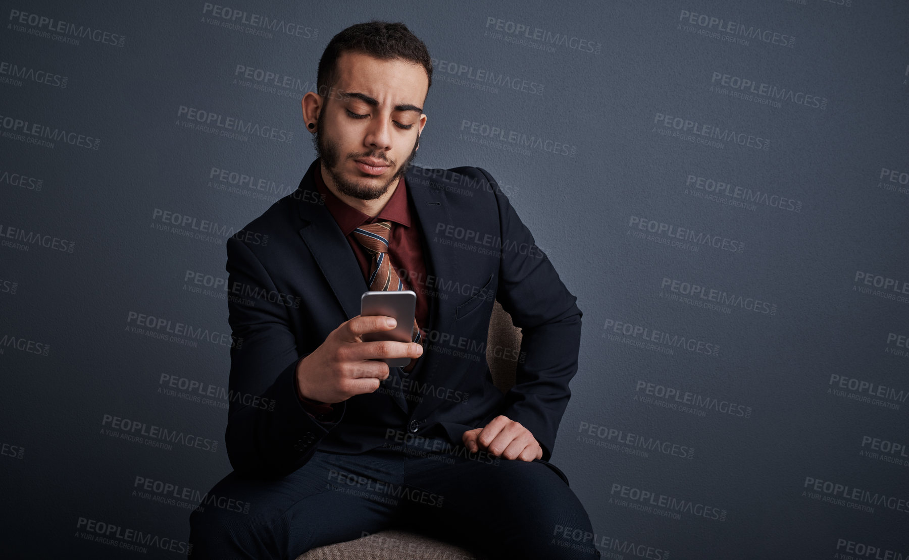 Buy stock photo Studio shot of a stylish young businessman sending a text message while sitting against a gray background