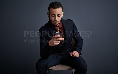 Buy stock photo Studio shot of a stylish young businessman sending a text message while sitting against a gray background