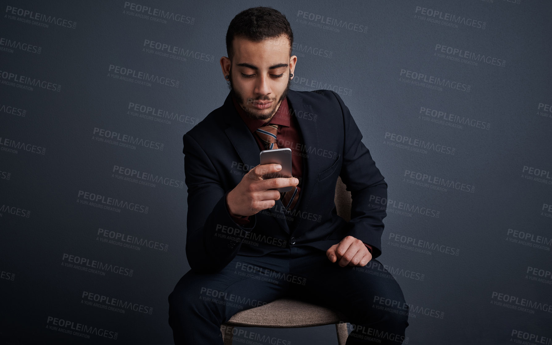 Buy stock photo Studio shot of a stylish young businessman sending a text message while sitting against a gray background