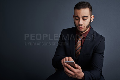 Buy stock photo Studio shot of a stylish young businessman sending a text message while sitting against a gray background