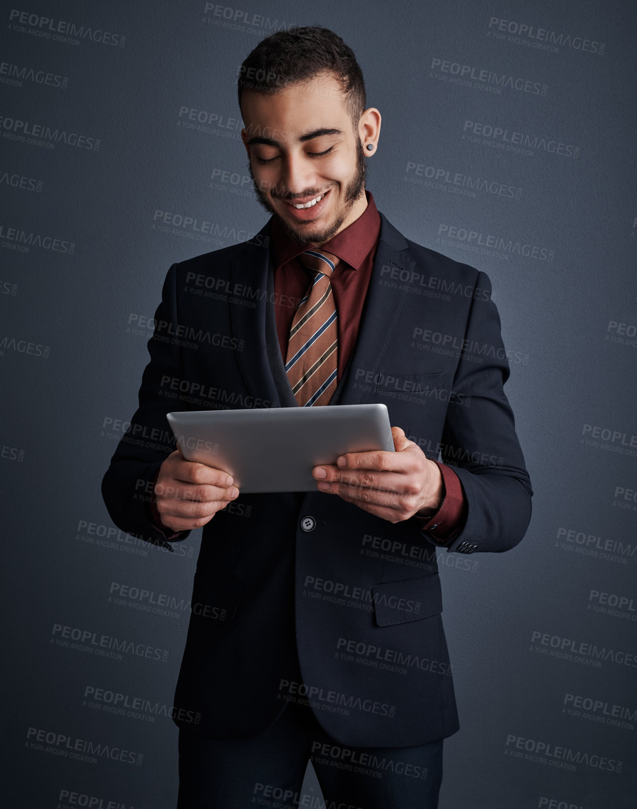 Buy stock photo Studio shot of a stylish young businessman using a tablet against a gray background