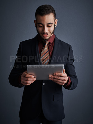 Buy stock photo Studio shot of a stylish young businessman using a tablet against a gray background