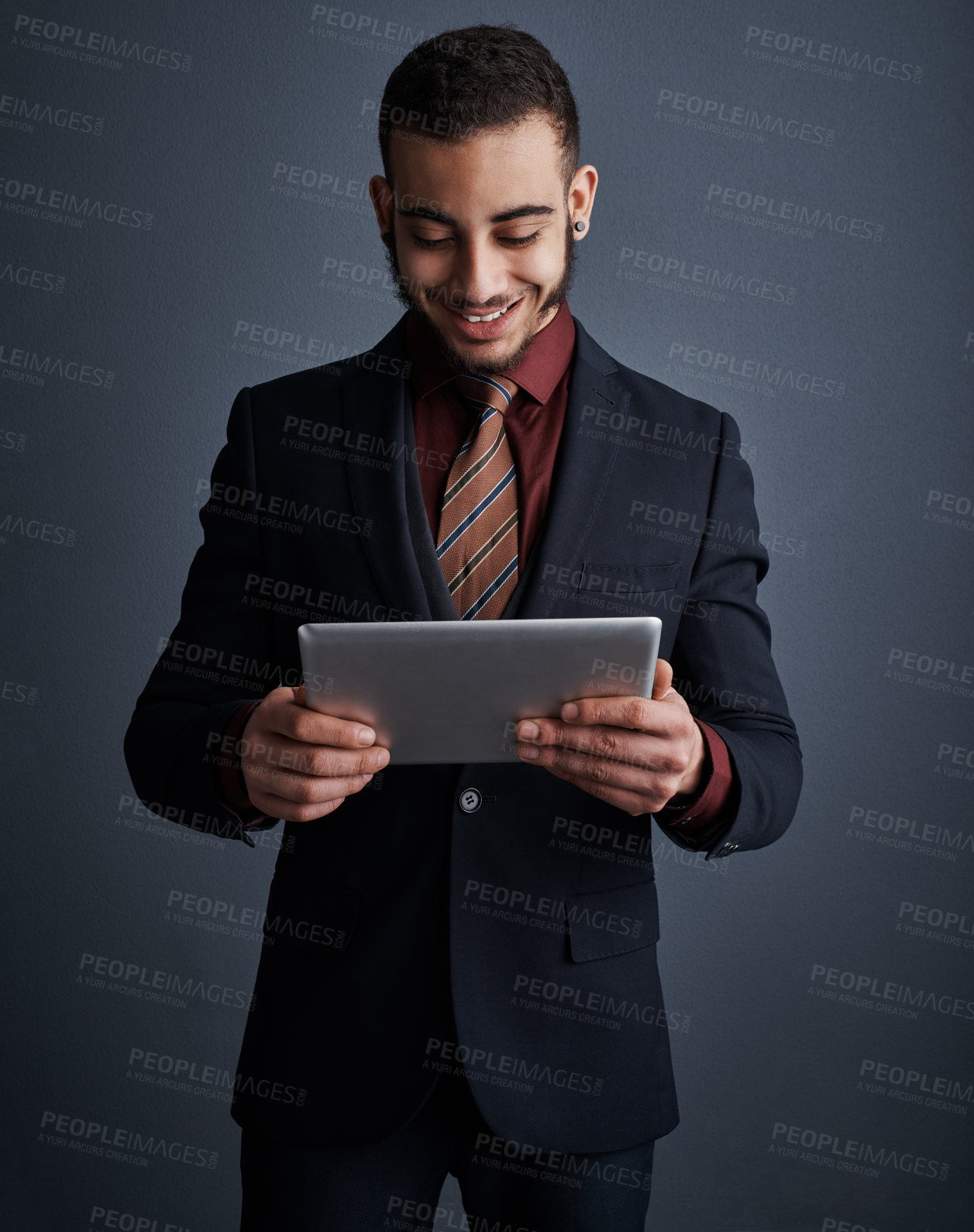 Buy stock photo Studio shot of a stylish young businessman using a tablet against a gray background