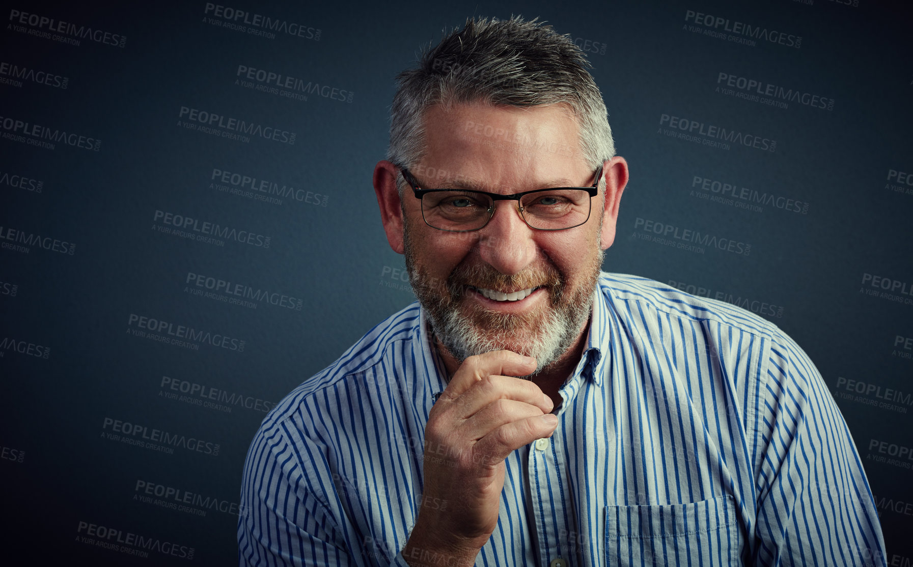 Buy stock photo Studio portrait of a confident and mature businessman sitting with his hand on his chin against a dark background