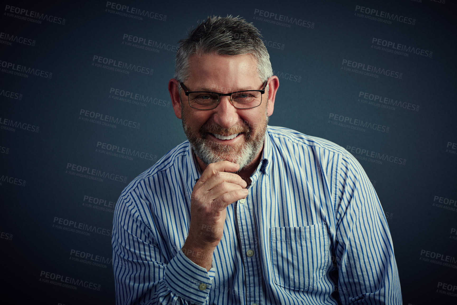 Buy stock photo Studio portrait of a confident and mature businessman sitting with his hand on his chin against a dark background