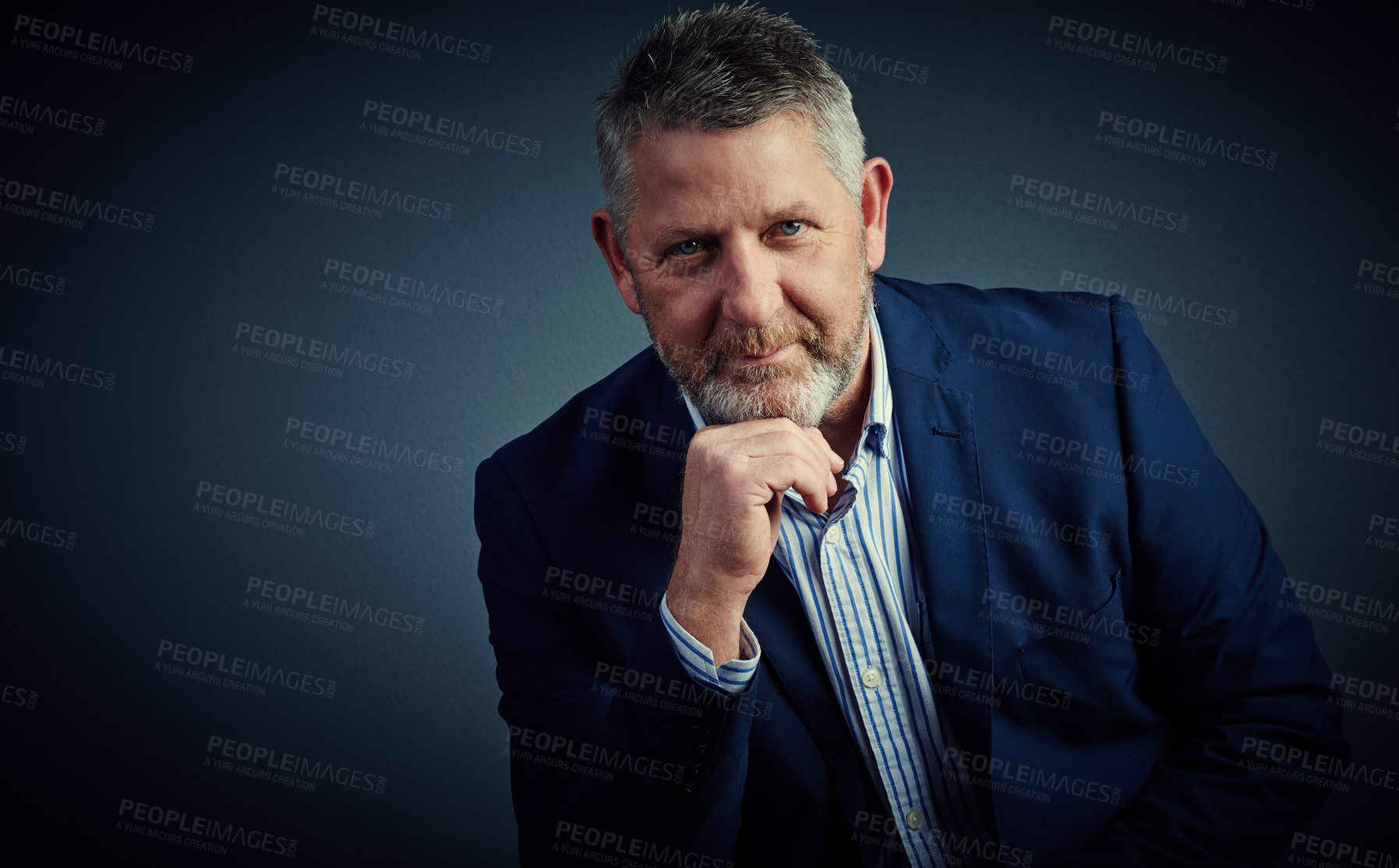 Buy stock photo Studio portrait of a confident and mature businessman sitting with his hand on his chin against a dark background