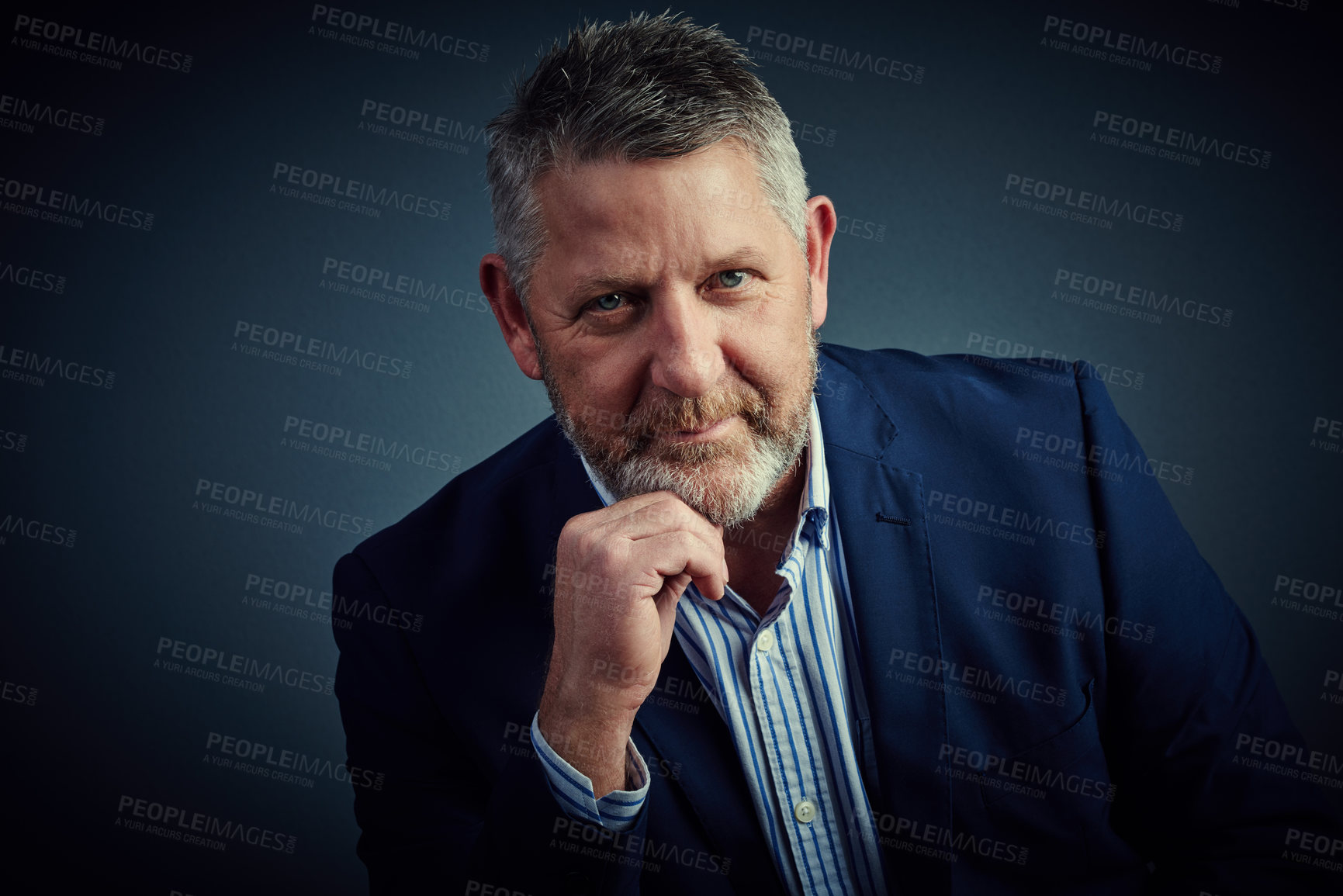 Buy stock photo Studio portrait of a confident and mature businessman sitting with his hand on his chin against a dark background