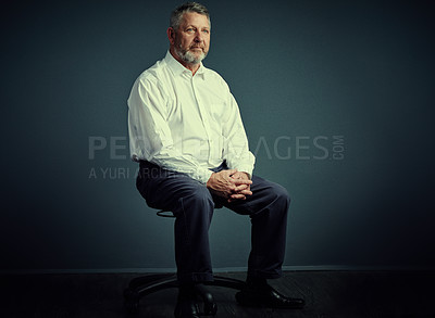 Buy stock photo Studio shot of a handsome mature businessman looking thoughtful while sitting down against a dark background