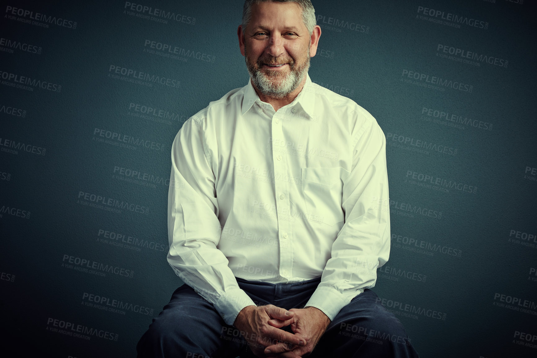 Buy stock photo Studio portrait of a handsome mature businessman sitting down against a dark background