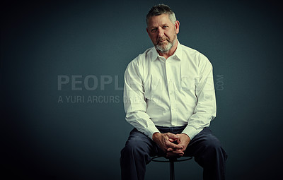 Buy stock photo Studio portrait of a handsome mature businessman sitting down against a dark background