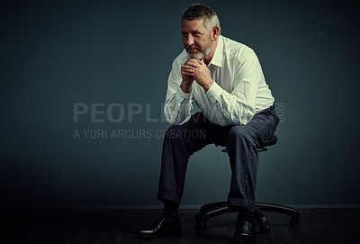 Buy stock photo Studio shot of a handsome mature businessman looking thoughtful while sitting down against a dark background