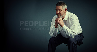 Buy stock photo Studio shot of a handsome mature businessman looking thoughtful while sitting down against a dark background