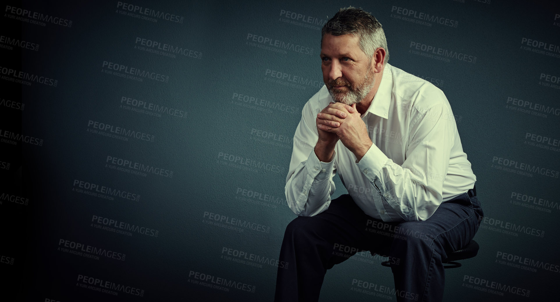 Buy stock photo Studio shot of a handsome mature businessman looking thoughtful while sitting down against a dark background