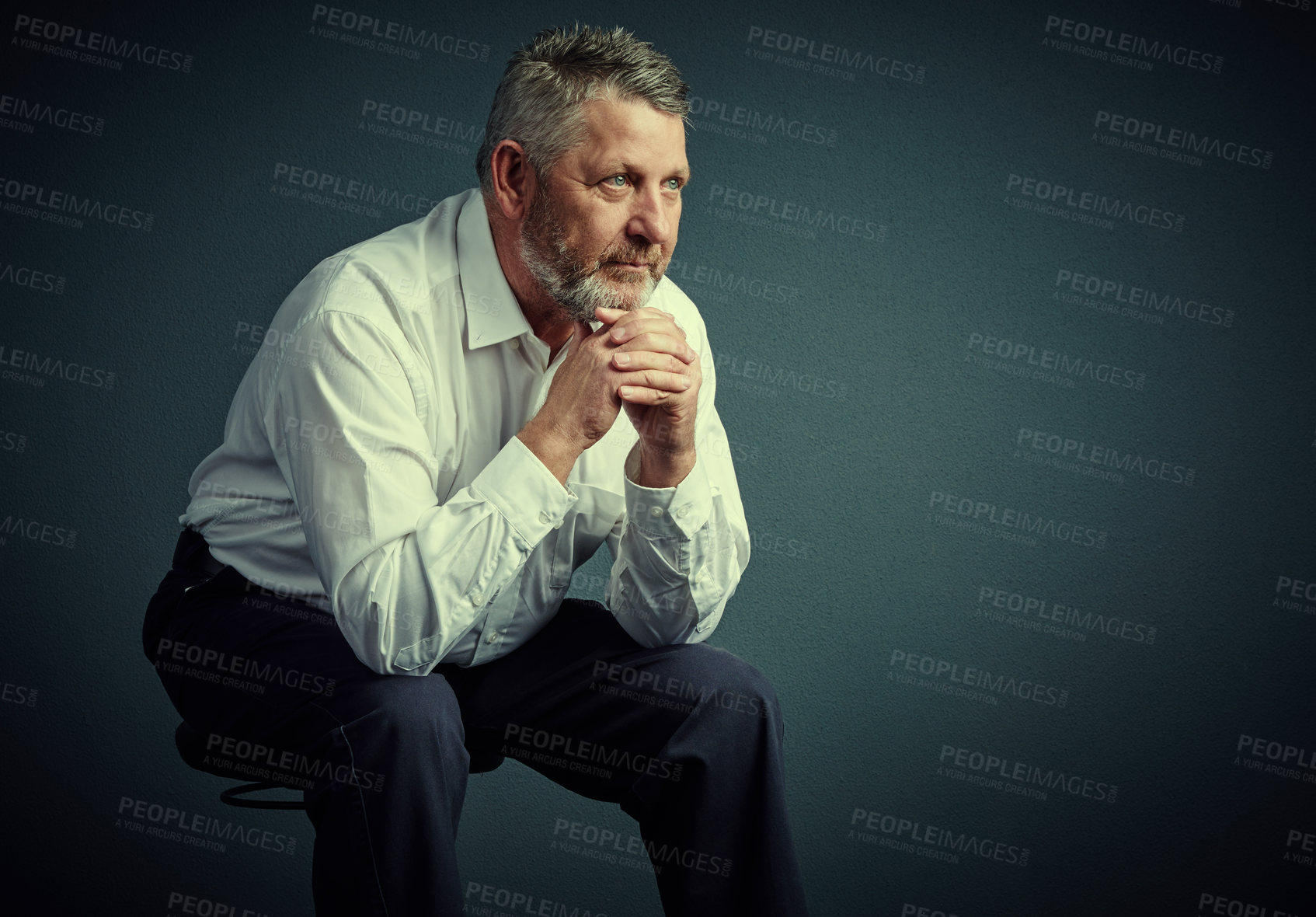 Buy stock photo Studio shot of a handsome mature businessman looking thoughtful while sitting down against a dark background