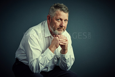 Buy stock photo Studio portrait of a handsome mature businessman looking thoughtful while sitting down against a dark background